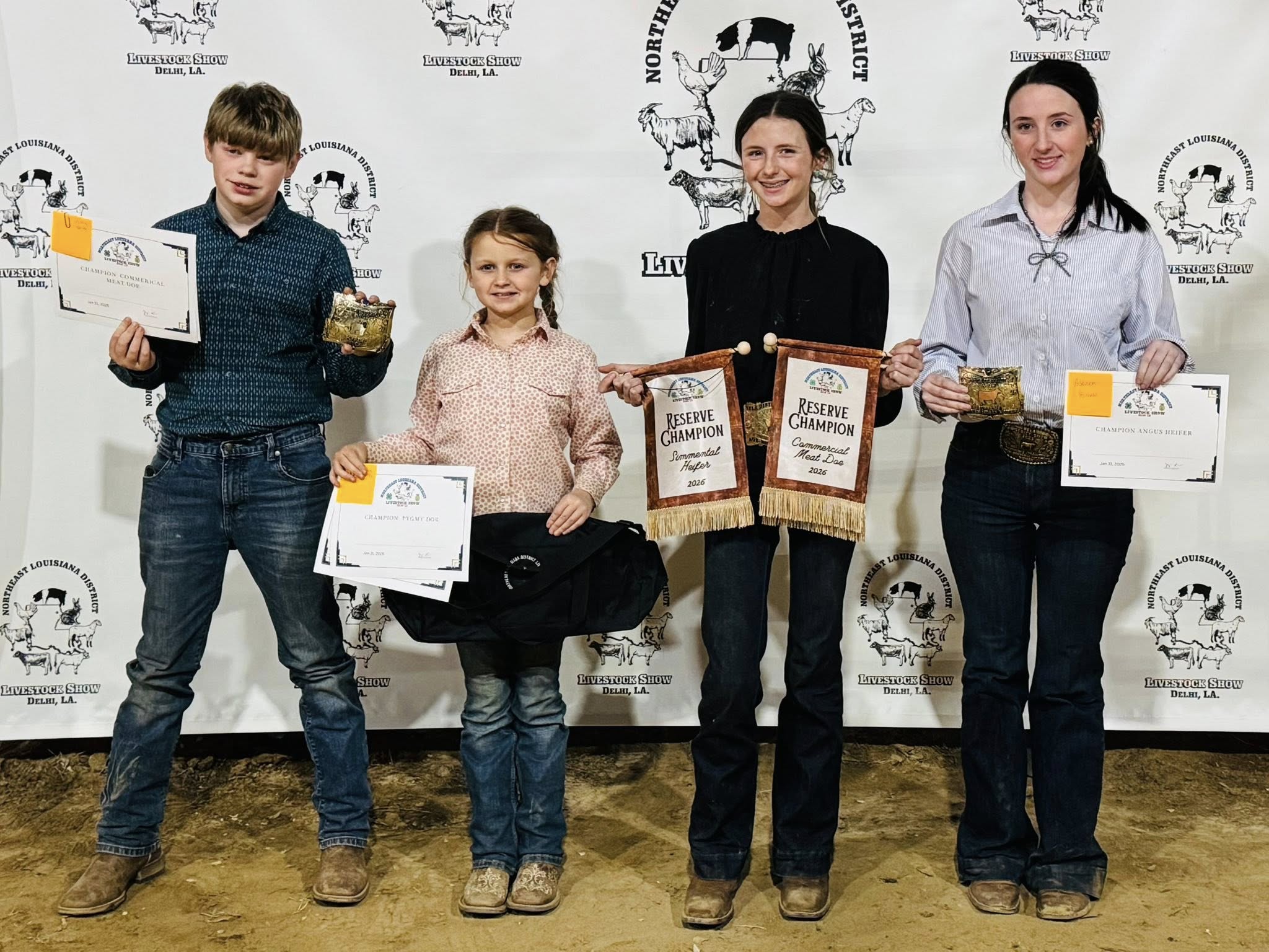 A boy and three girls holding awards and belt buckles.